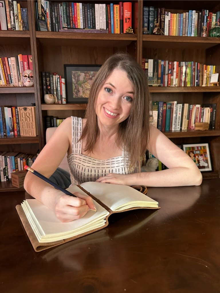 Diane is a white woman with long light brown hair. She is writing in a book - she is holding a pencil