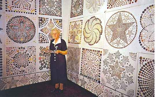 Frieda Wartha stands against walls covered with remarkable button mosaics. 