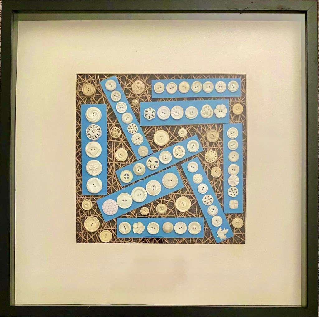 Button on strips of blue or against a brown background, framed. The detail of each button is different but all are small and cream. 